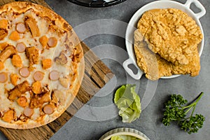 Top view shot of delicious tasty juicy sliced sausage cheesy pizza placed on wooden board around with other fast food crispy fried