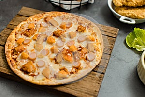 Top view shot of delicious tasty juicy sliced sausage cheesy pizza placed on wooden board around with other fast food crispy fried