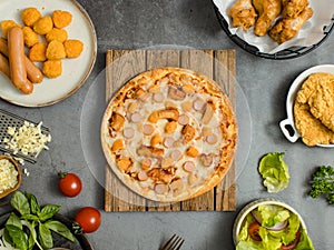 Top view shot of delicious tasty juicy sliced sausage cheesy pizza placed on wooden board around with other fast food crispy fried