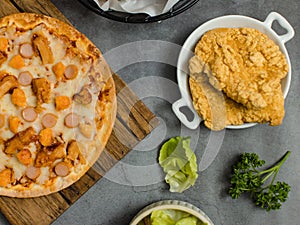 Top view shot of delicious tasty juicy sliced sausage cheesy pizza placed on wooden board around with other fast food crispy fried