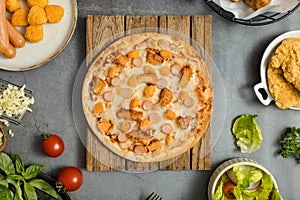 Top view shot of delicious tasty juicy sliced sausage cheesy pizza placed on wooden board around with other fast food crispy fried