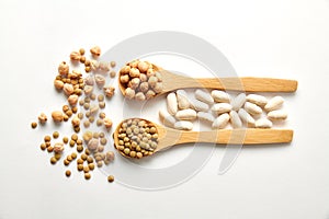 Top view shot of dried lentils, chickpeas, and white beans with wooden spoons on white background