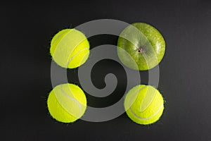 Top view shot of a green apple and three tennis balls in the black background