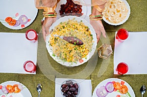 Top view shot of indian woman hands placing chicken biryani plate on table during ramadan dinner at home - concept of