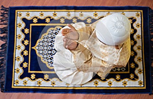 Top view shot of muslim kid doing namaz during ramadan feast celebration at home.