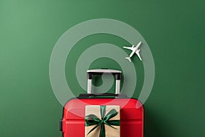 Top view shot of a suitcase, miniature airplane model, and craft paper giftbox on green background
