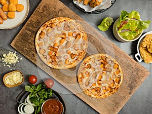 Top view shot of two delicious tasty juicy sliced sausage cheesy pizza placed on wooden board around with other fast food crispy