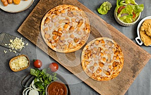 Top view shot of two delicious tasty juicy sliced sausage cheesy pizza placed on wooden board around with other fast food crispy