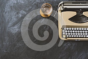 Top view shot of typewriter and a glass of water on blackboard background