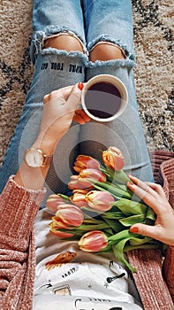 Top view shot of a woman holding a bunch of tulips and a cup of black coffee