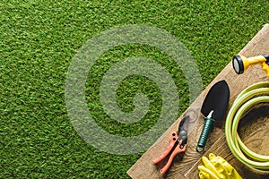 top view of shovel, secateurs, protective gloves and hosepipe on wooden