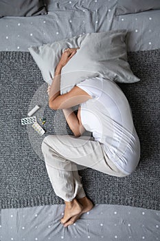 Top view of sick mature woman lying in bed suffering