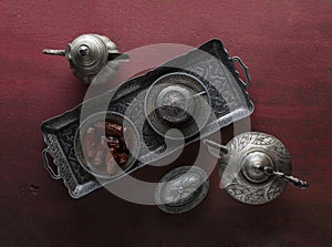 Top view on silver plate with dates and coffee cup on the dark red wooden background. Ramadan background. Selective focus