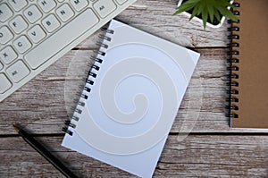Top view of simple office desk with computer keyboard, pen and blank notepad.