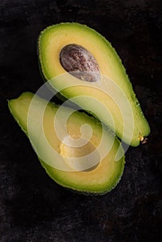 Top view on single avocado severed in half on black tray