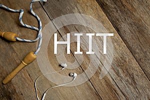 Top view of skipping rope and earphone on wooden background written with HIIT. Health and fitness concept.