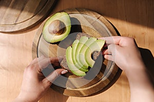 Top view of sliced avocado on dark bread on wooden table. Second half of avocado with pit