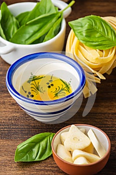 Top view of sliced garlic, olive oil and basil with raw tagliatelle, on wooden table