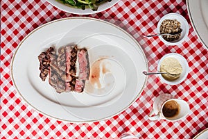Top view of Sliced medium rare charcoal grilled wagyu Ribeye steak in white plate on red and white pattern tablecloth with cutlery