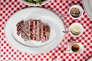 Top view of Sliced medium rare charcoal grilled wagyu Ribeye steak in white plate on red and white pattern tablecloth.