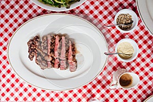 Top view of Sliced medium rare charcoal grilled wagyu Ribeye steak in white plate on red and white pattern tablecloth.