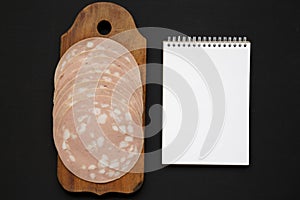 Top view, sliced Mortadella Bologna Meat on a rustic wooden board over black background, top view. Flat lay, from above, overhead
