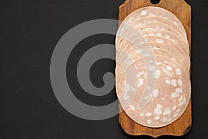 Top view, sliced Mortadella Bologna Meat on a rustic wooden board over black surface. Flat lay, from above, overhead. Copy space