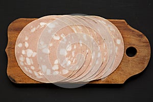 Top view, sliced Mortadella Bologna Meat on a rustic wooden board over black surface, top view. Flat lay, from above, overhead.