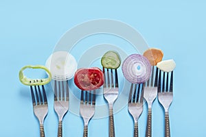 Top view of sliced pieces of fresh vegetables and spices on forks against a blue background