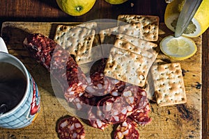 Top view of sliced salami, biscuits, lemons, and a cup of coffee on a wooden chopping board