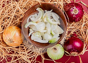 top view of sliced white onion in bowl with sweet, red and whole white one on straw and red background