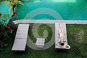 Top view of slim woman in beige bikini take sunbath on lounge chair at the poolside near luxury pool in tropic on vacation
