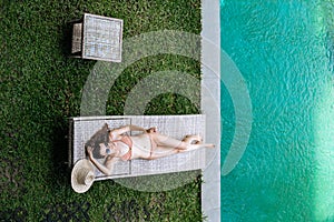 Top view of slim woman in beige bikini take sunbath on lounge chair at the poolside near luxury pool in tropic on vacation