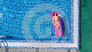 Top view of slim young woman in bikini on the air mattress in the big swimming pool. Enjoying sunmtan. Vacation concept