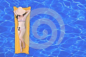 Top view of slim young woman in bikini relaxing on the yellow air mattress in swimming pool