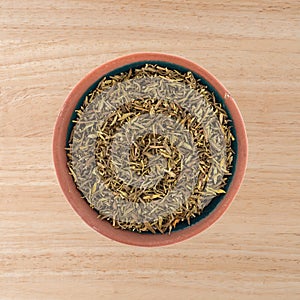 Top view of a small bowl with a portion of organic thyme leaf on a wood tabletop