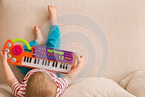 Top view on small cute toddler boy sitting on the sofa and playing on the toy piano. A little boy learning to play piano listening
