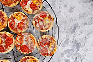 Top view of small mini pizzas topped with cheese, tomato, yellow and red bell peppers and salami sausage on round black grid