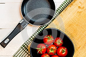 Top view of small pan and fresh ripe cherry tomatoes in small black bowl on a rustic white wooden table. Ingredients and food