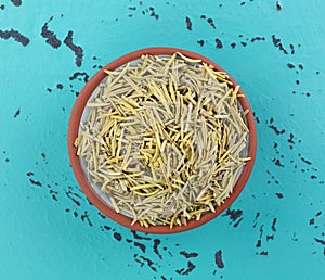 Top view of a small terracotta bowl filled with rosemary whole leaf on a tabletop