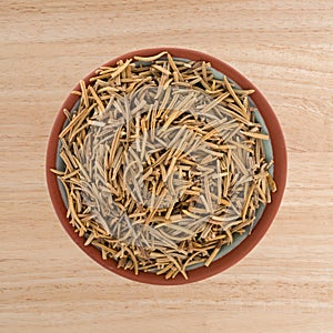 Top view of a small terracotta bowl filled with rosemary whole leaf on a wood tabletop