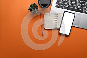 Top view of smart phone, notebook, coffee cup and laptop on orange background.