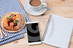 top view of Smart phone with notebook and cup of latte art coffee on wooden background.