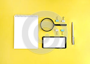 Top view of smart phone, notepad and stationery on yellow background. Information or job searching.