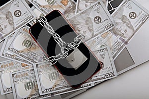 Top view of smartphone locked by chain with padlock on a dollar banknotes. Cyber crime concept