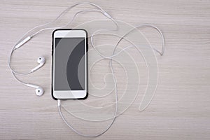 Top view of a smartphone with plugged earphones on a wooden table