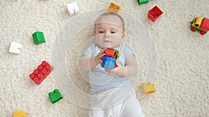 Top view of smiling baby boy lying on carpet in playroom with lots of colorful toys. Concept of children development