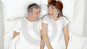 Top view of smiling couple having fun in bed hiding under blanket and looking into camera.