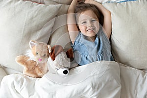 Top view smiling cute girl lying in bed with toys