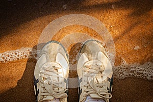 Top view sneakers on sand beach surrounded with clear sea water and shadow of tree in vintage style.